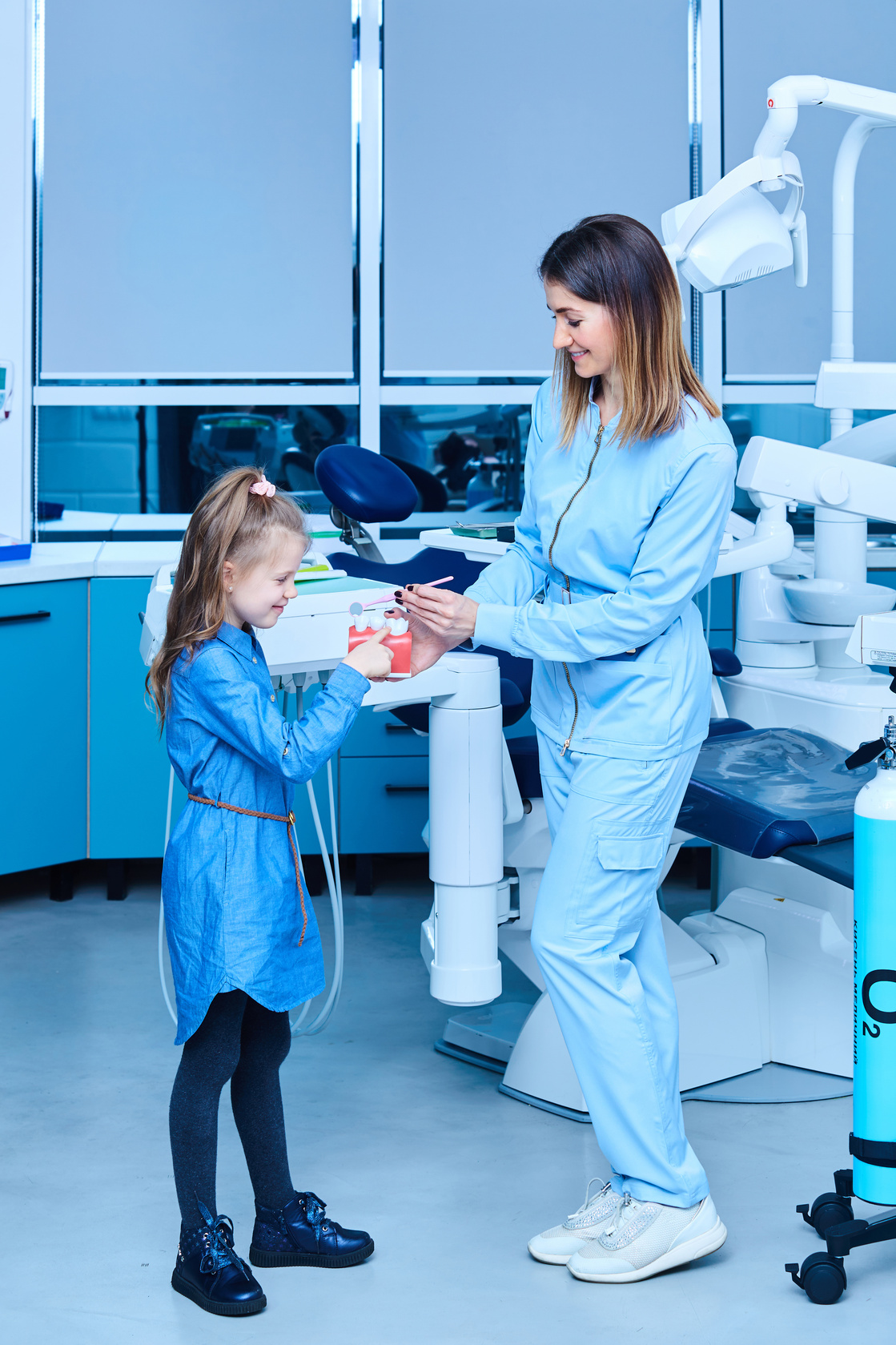 Pediatric dentist showing basic dental hygiene principles. Female pediatric dentist showing a treatment for adorable little girl in a hospital. Dentist and child in cabinet. Little girl in the dentists office